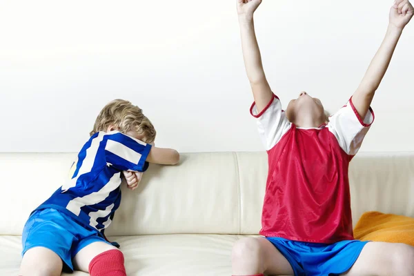 Двое детей поддержки разных команд, смотреть футбол и отмечать у себя дома — стоковое фото