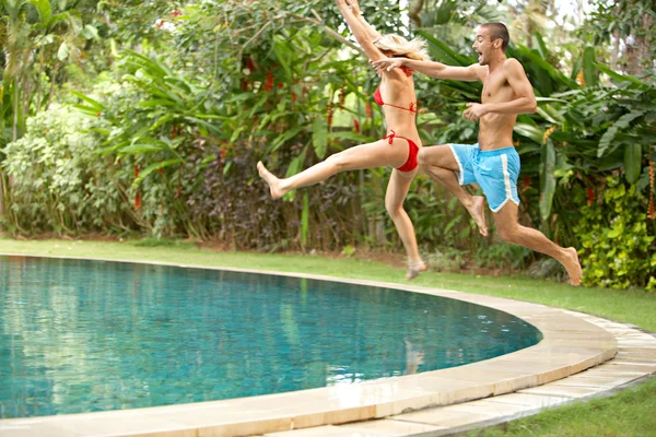 Молодые весело пара прыжков в тропический бассейн — стоковое фото