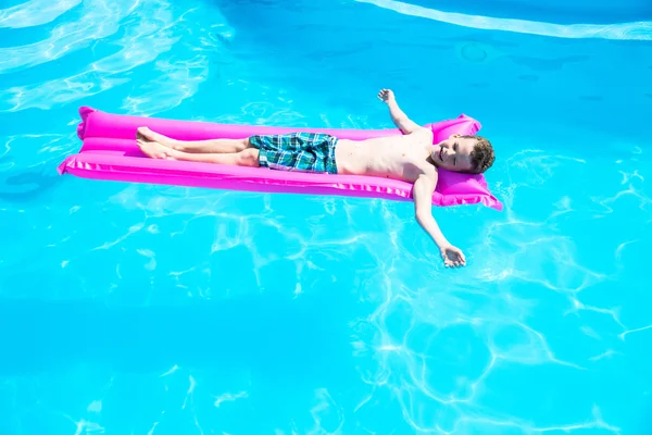 Мальчик плавает на надувном матрасе в бассейне — стоковое фото
