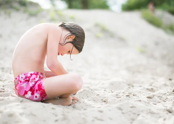 Маленькая девочка в розовых трусиках, сидя на песке на пляже на жаркий летний день — стоковое фото
