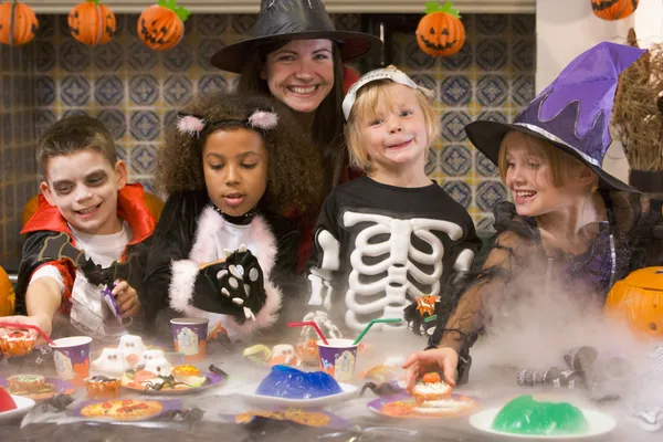 Четыре молодых друзей и женщина на Хэллоуин, едят сладости и sm — стоковое фото